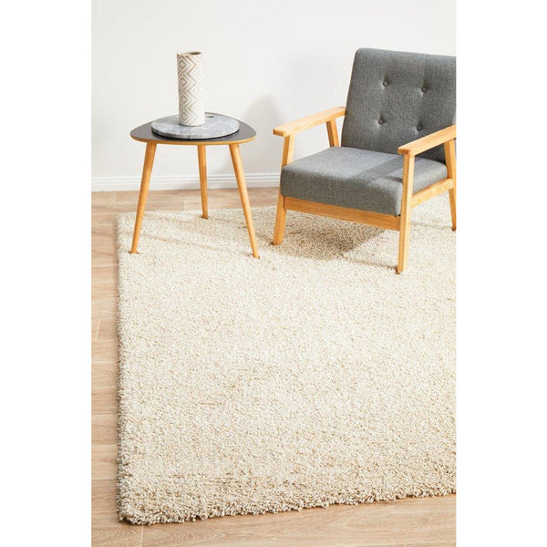 Cream shaggy rug with thick polypropylene pile under a gray cushioned wooden armchair and a round wooden side table with a vase.