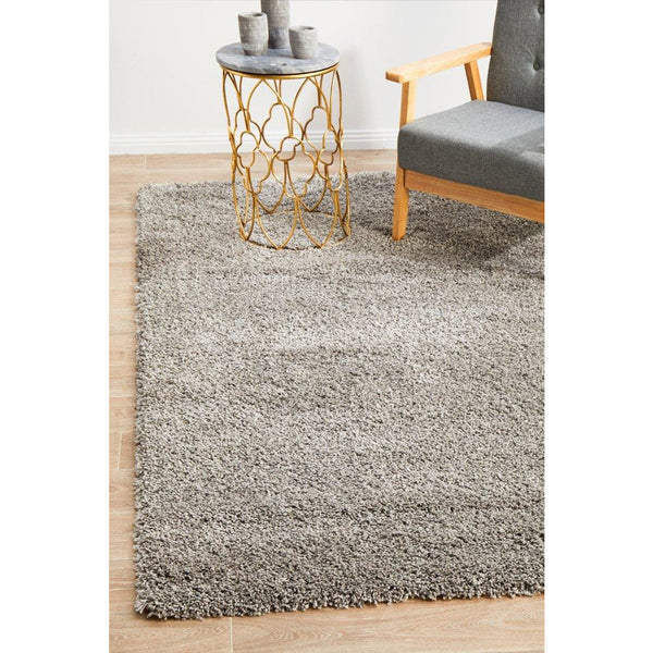 Silver grey shaggy rug with dense pile on light wood floor, partially under a modern chair and round metal side table.