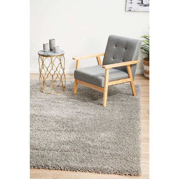 Silver grey modern shaggy rug with thick polypropylene pile under grey upholstered wooden armchair and gold metal side table.
