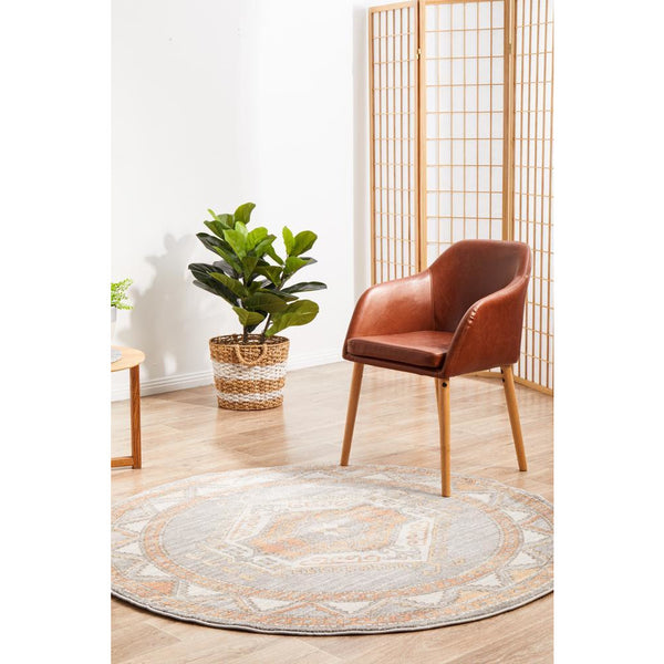 Round peach grey rug with medallion pattern, placed next to a brown leather chair and woven plant basket.