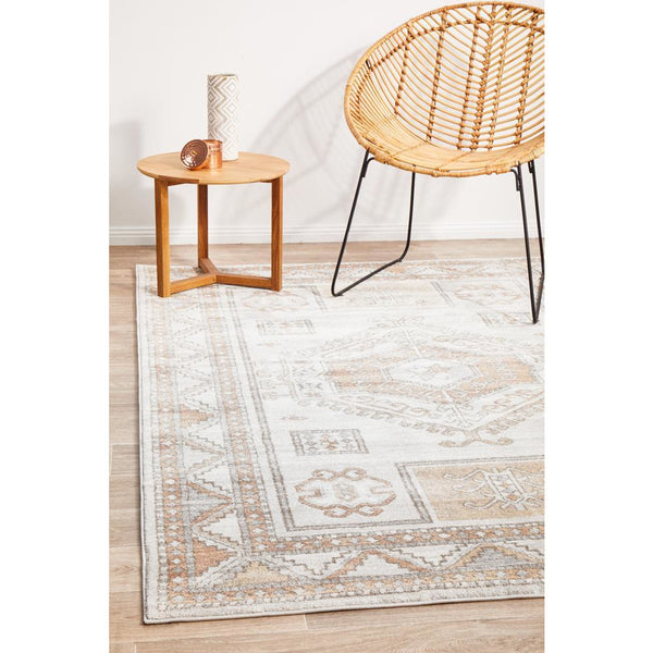 Transitional medallion patterned rug in peach, natural white, and silver tones with geometric border on light hardwood floor.