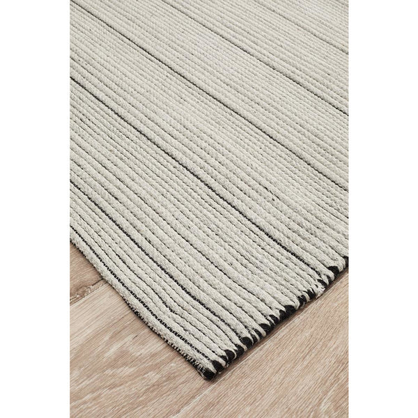 Beige striped flatweave rug with textured cotton and wool fibers on wooden floor.