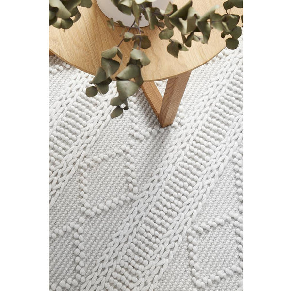 Ivory wool blend rug with textured geometric and diamond patterns under wooden table legs.
