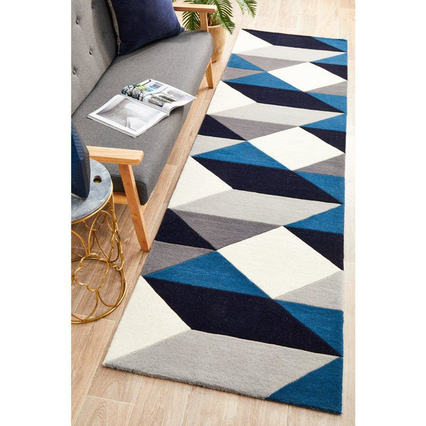 Blue, grey, navy, and white geometric pattern wool runner rug on wooden floor beside grey cushioned bench.