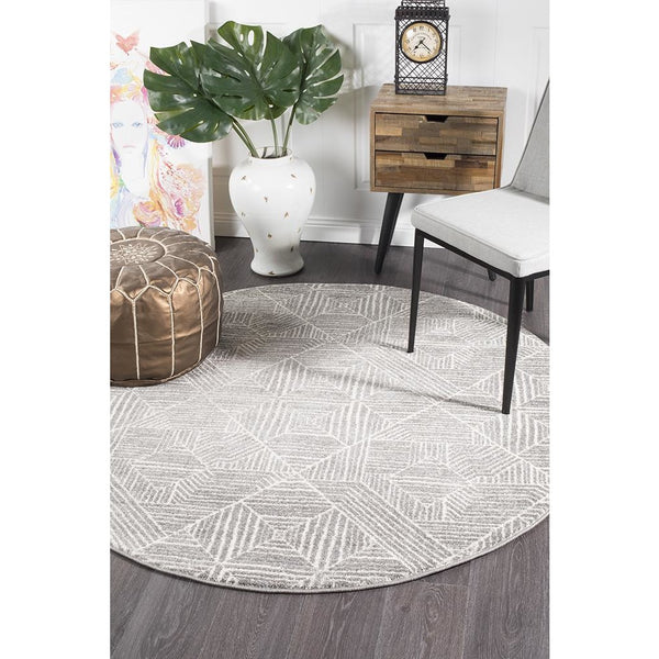 Round silver grey tribal patterned rug with textured geometric designs on dark wood floor.