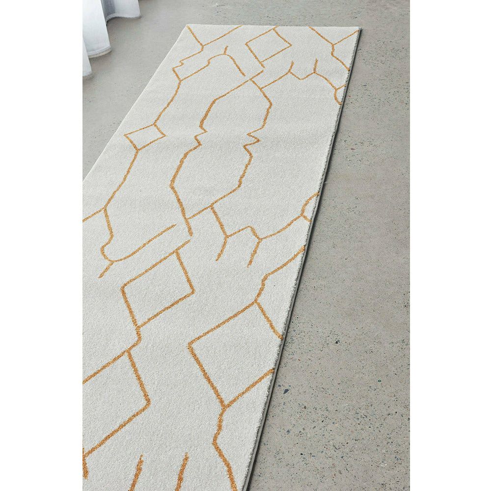 Long cream runner rug with abstract gold geometric lines on concrete floor.