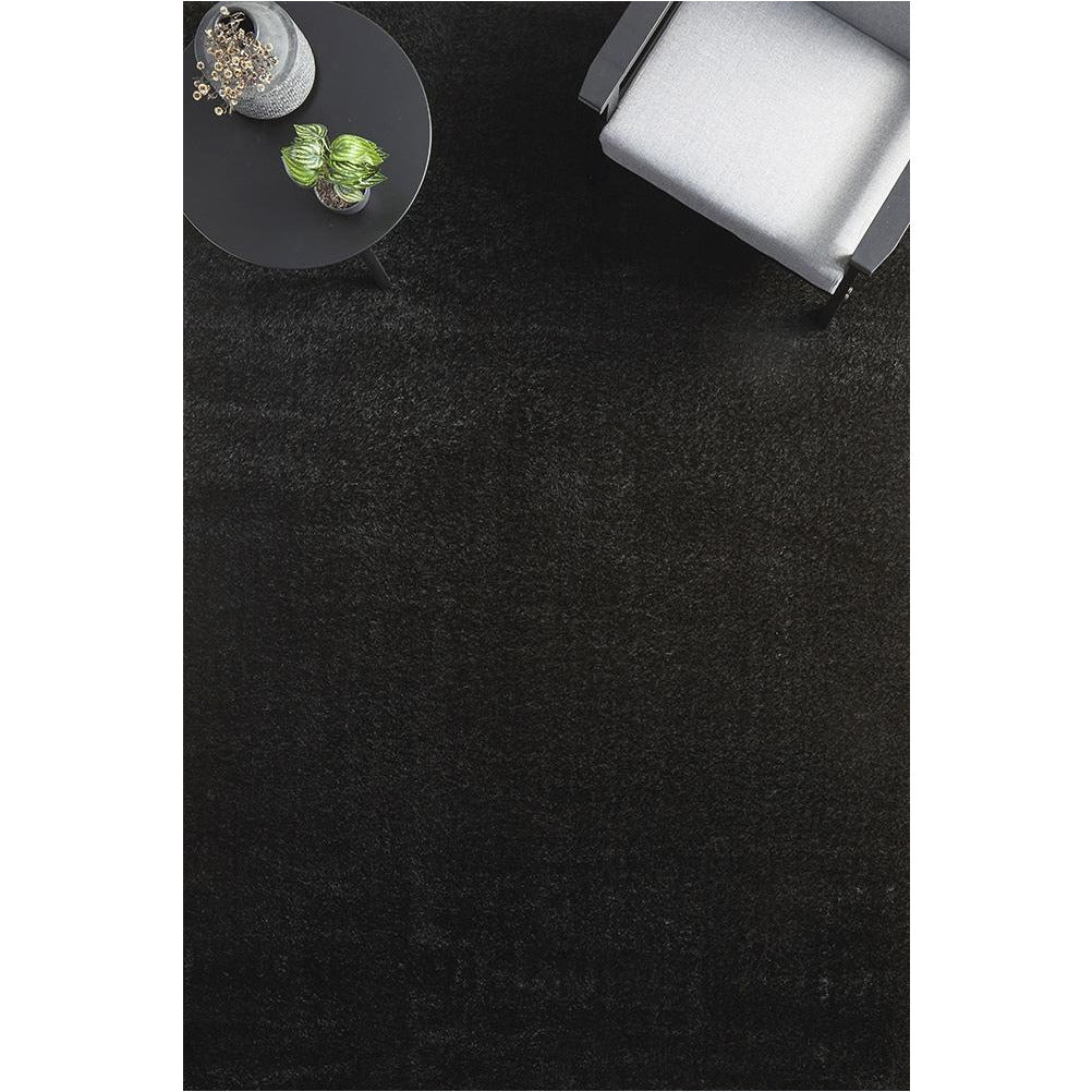 Black soft shaggy modern rectangular rug with 50mm pile under gray armchair and round black side table.