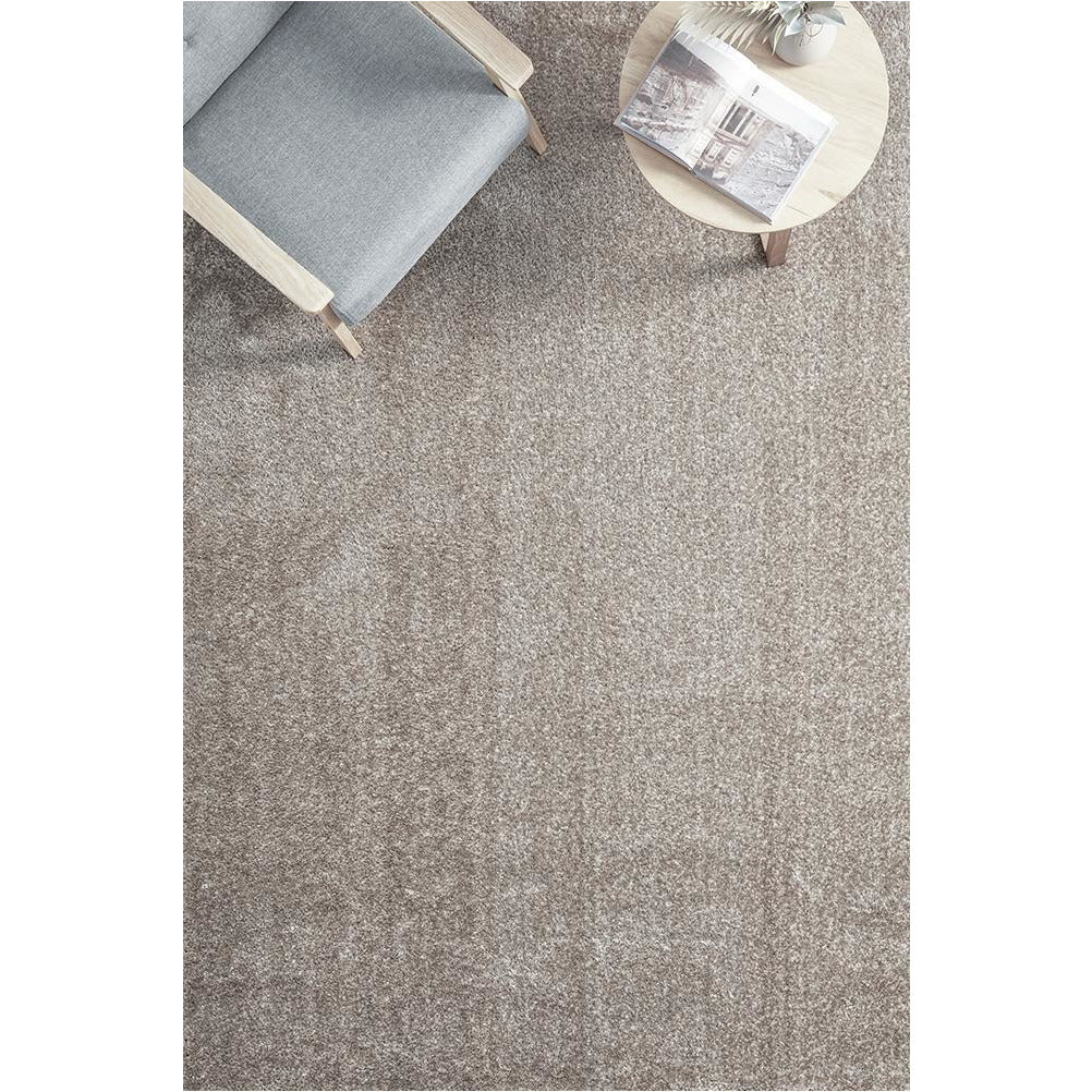 Rectangular beige mink modern soft shaggy rug under gray armchair and round wooden side table.