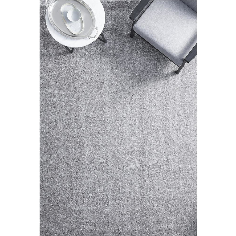Silver grey soft shaggy rectangular rug with plush polyester pile under modern gray chair and white round side table.