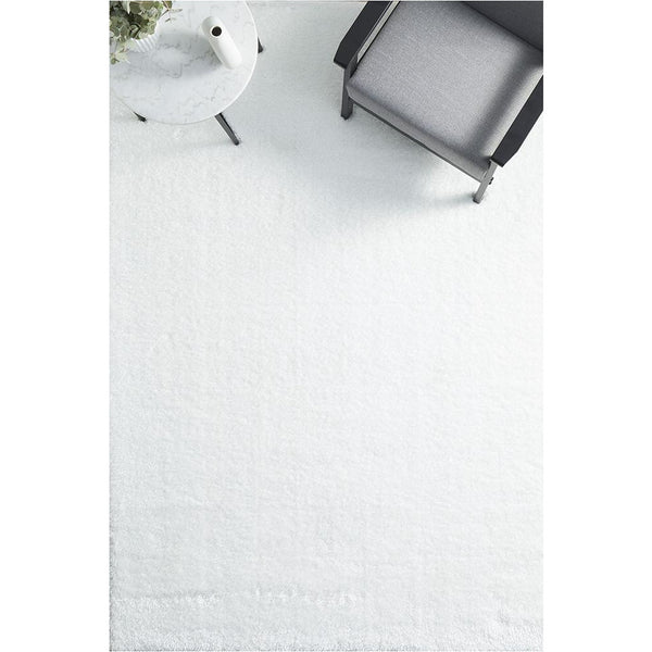Ivory white modern soft shaggy rectangular rug under gray armchair and white side table.
