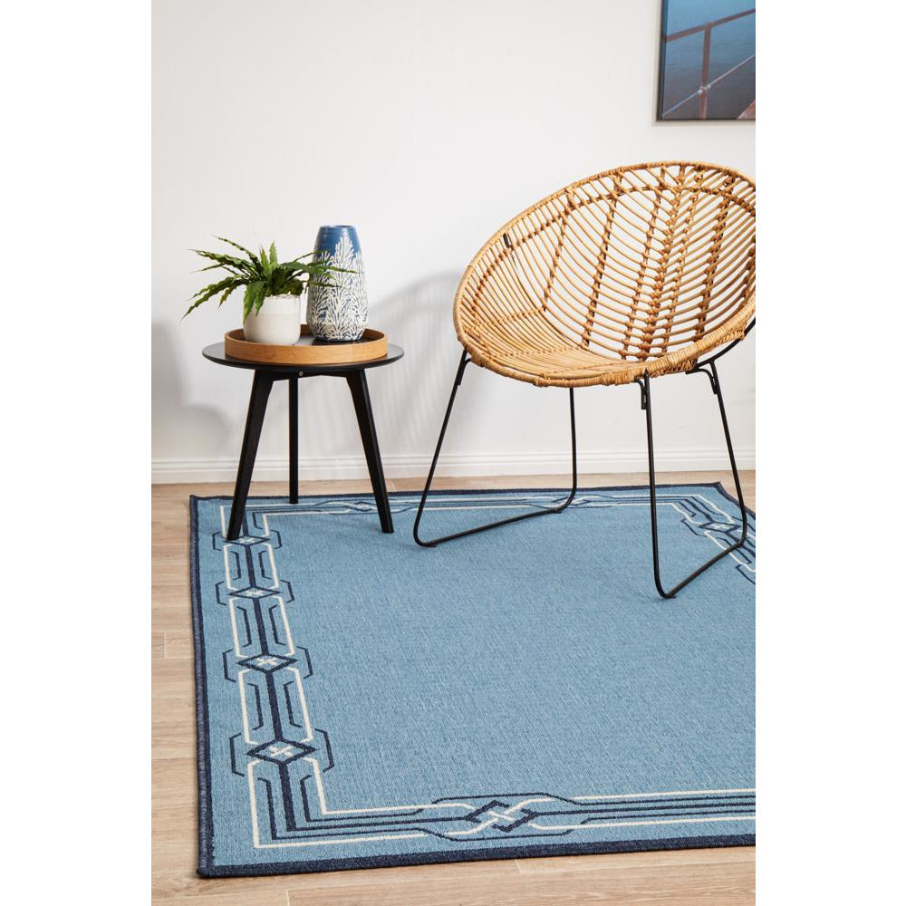 Blue rectangular rug with geometric border pattern on light floor.