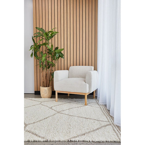 Neutral-toned wool blend rug with subtle geometric diamond pattern under a light gray armchair and potted plant.