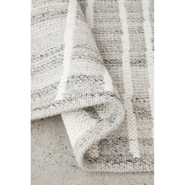 Neutral-toned wool blend rug with subtle striped pattern and flat-woven texture, corner folded.
