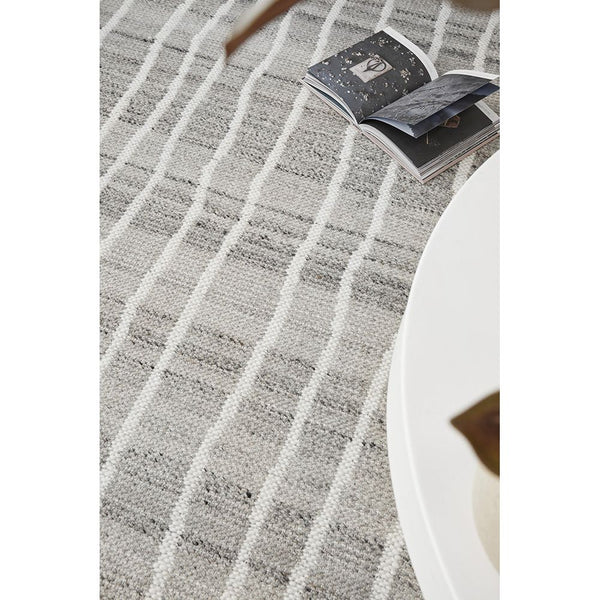 Gray and white flat-woven wool rug with a linear geometric pattern under a white round table with an open book on the rug.