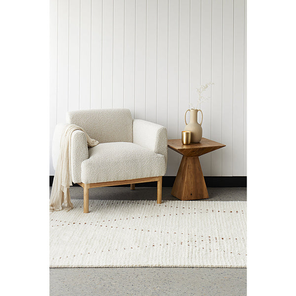 Natural wool and cotton flatwoven rug in neutral tones with subtle geometric pattern under beige armchair and wooden side.