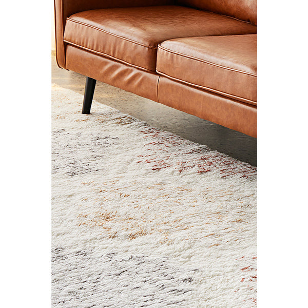 Soft wool-cotton rug with a modern multicolor patterned design under a brown leather sofa leg.