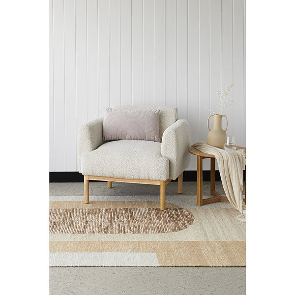 Natural flatwoven wool and cotton rug with geometric patterns in beige and cream tones under a light armchair with wooden.